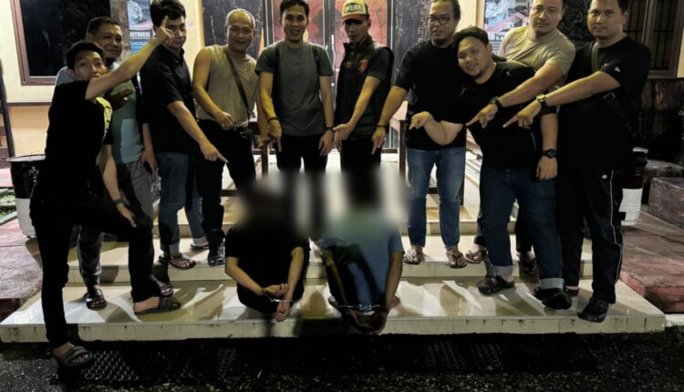 Anggota Reskrim Polsek Sanga Desa mengamankan dua tersangka pencurian dengan pemberatan berinisial PI dan RG (duduk dengan tangan terborgol) di depan Markas Polsek Sanga Desa, Musi Banyuasin, Sumatra Selatan.